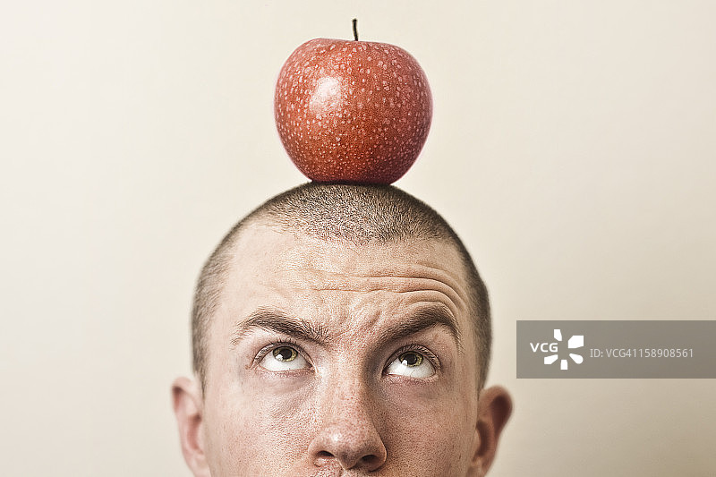 头上顶着一个红苹果的男人。图片素材