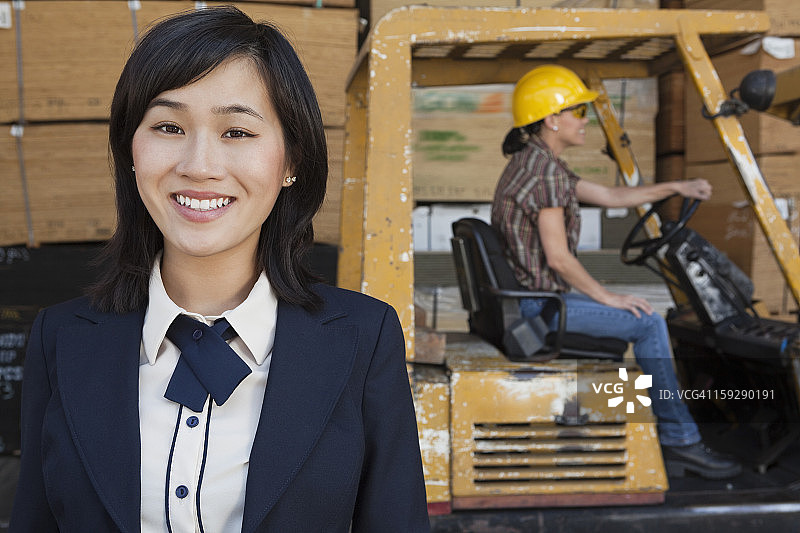 妇女微笑的肖像，而女性产业工人驾驶叉车在背景图片素材
