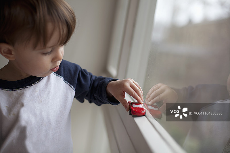 一个小男孩推着一辆玩具车沿着窗台走图片素材