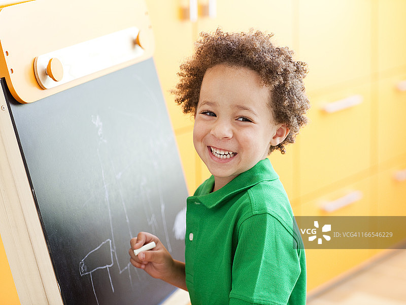一个小男孩拿着粉笔站在小黑板旁边图片素材