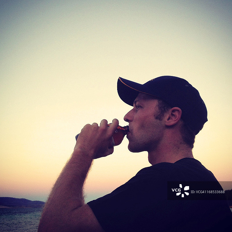 日落时分在海滩附近喝酒的男人图片素材
