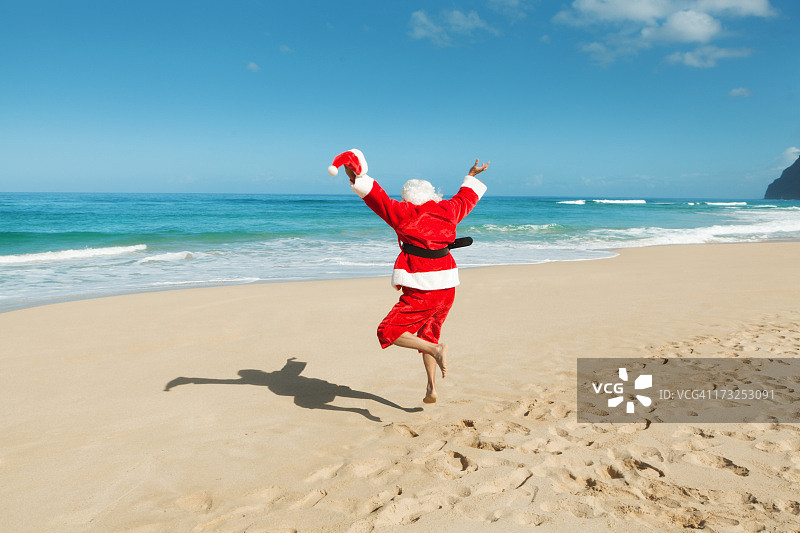 快乐兴奋跳跃的圣诞老人在热带海滩度假图片素材