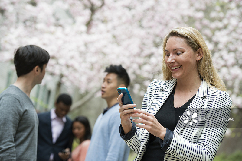 春天的城市生活。年轻人在城市公园的户外活动。一个女人在用手机，背景是四个人，男人和女人。图片素材
