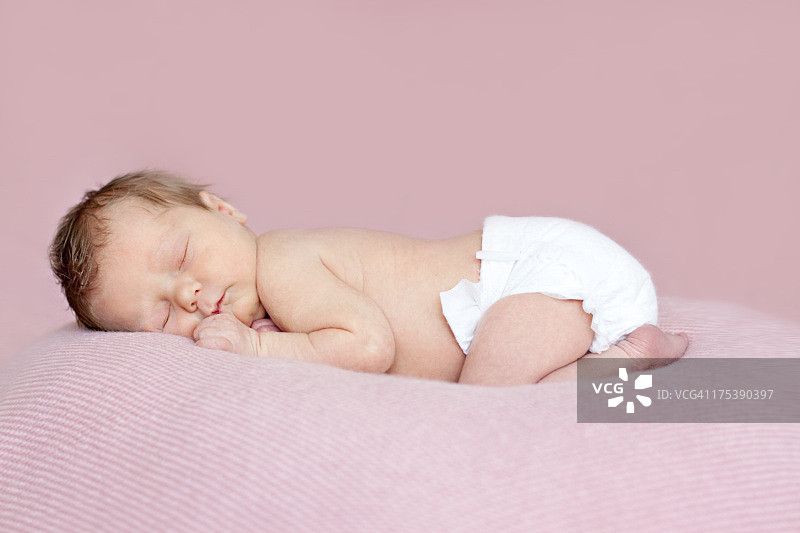 丰满的新生女婴俯卧着睡着。粉红色的背景。图片素材