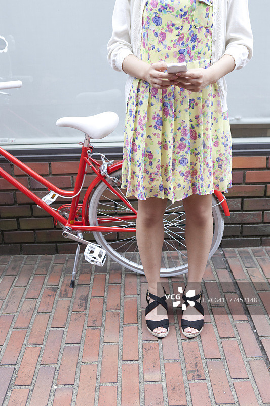 女人拿着智能手机，站在自行车前图片素材