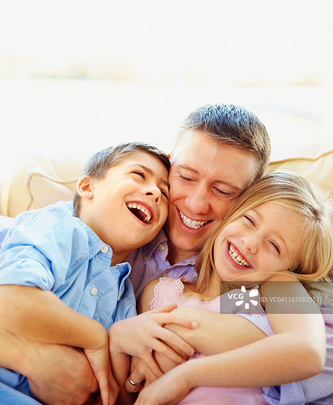 快乐的父亲和两个孩子在沙发上玩图片素材