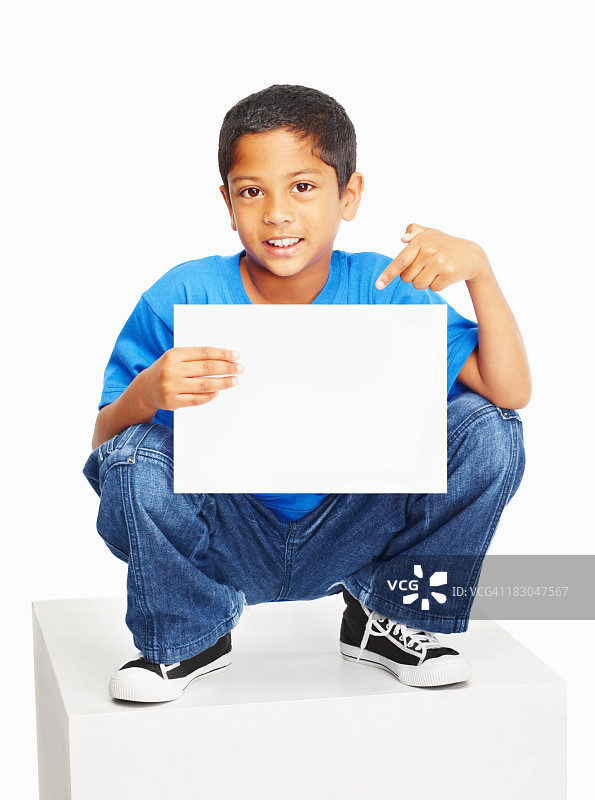 一个无辜的男孩坐在白色的立方体上指着文案图片素材
