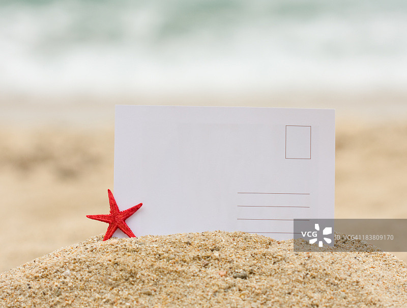 一张空白的明信片卡在一堆沙子里，旁边是一只海星图片素材