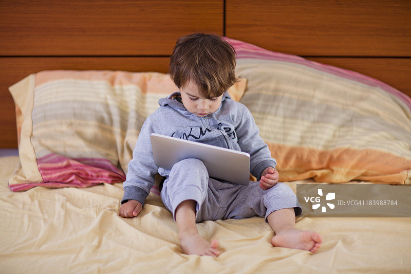 小男孩在床上看平板电脑图片素材