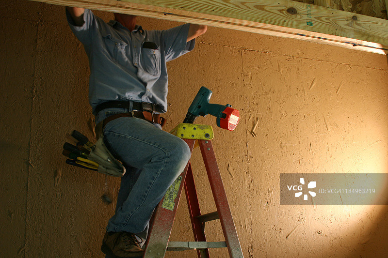 白人电工在梯子上带着工具带在壁橱里工作图片素材