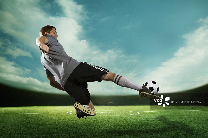 足球运动员在半空中踢着足球，在体育场里与天空一起飞翔图片素材