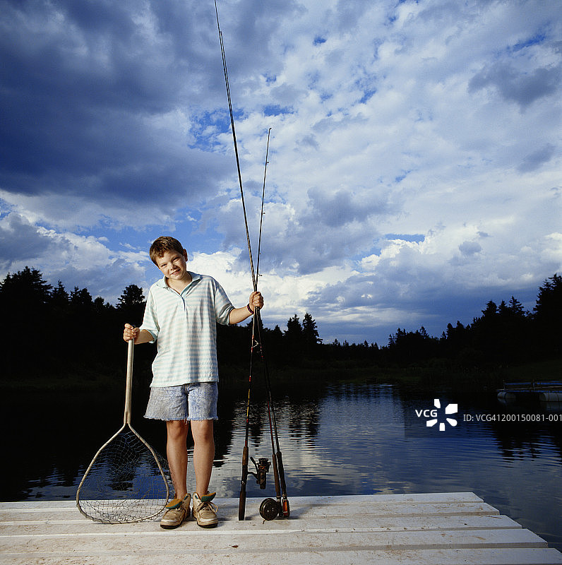 男孩(9-11)在码头上拿着钓竿和网，肖像图片素材