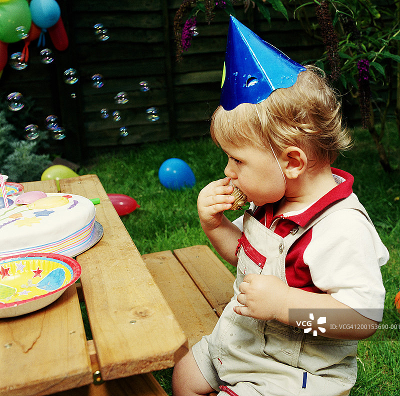 宝宝(12-15个月)戴派对帽，在户外吃蛋糕图片素材