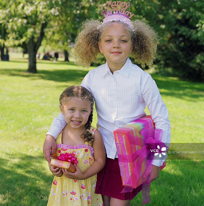 姐妹(3-7)在公园举行生日聚会，拿着礼物、画像图片素材