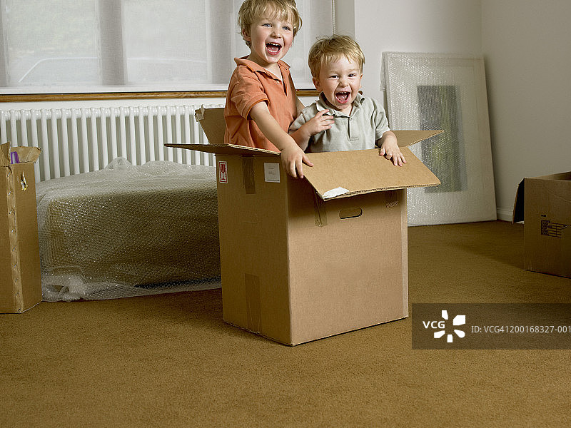 两兄弟(21个月-4岁)在纸板箱里玩，笑着图片素材
