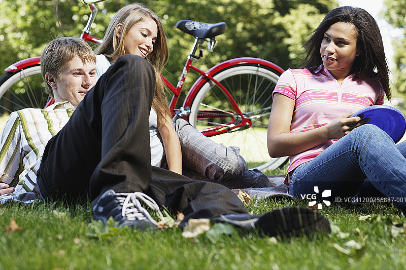年轻的男人，女人和少女坐在草地上与飞盘图片素材