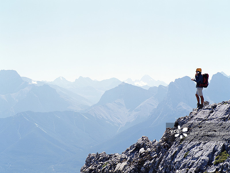 成熟的男性登山运动员在山顶上使用手机，侧视图片素材