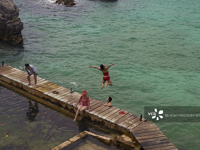 两对夫妇在码头上休息，一名女子跳入水中，俯瞰高处图片素材