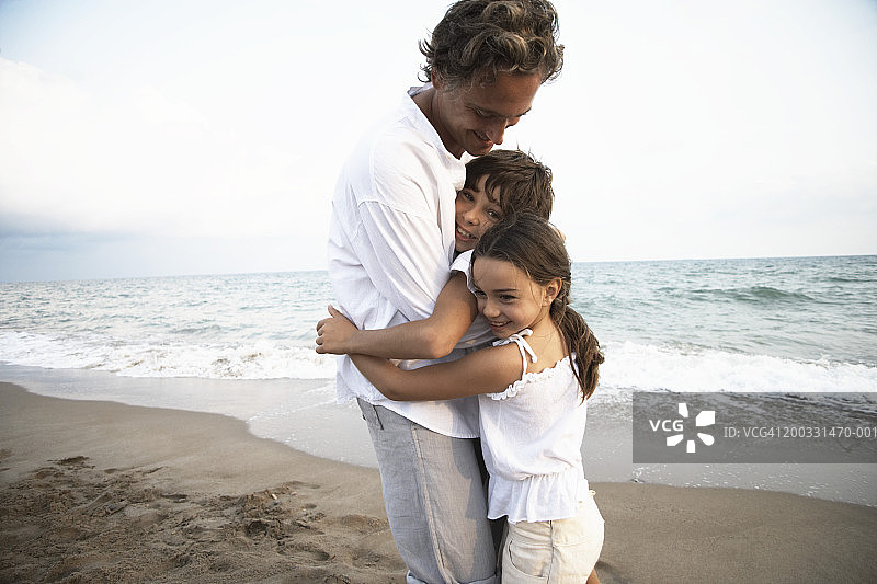 父亲在海滩上拥抱儿子(8-10)和女儿(6-8)图片素材