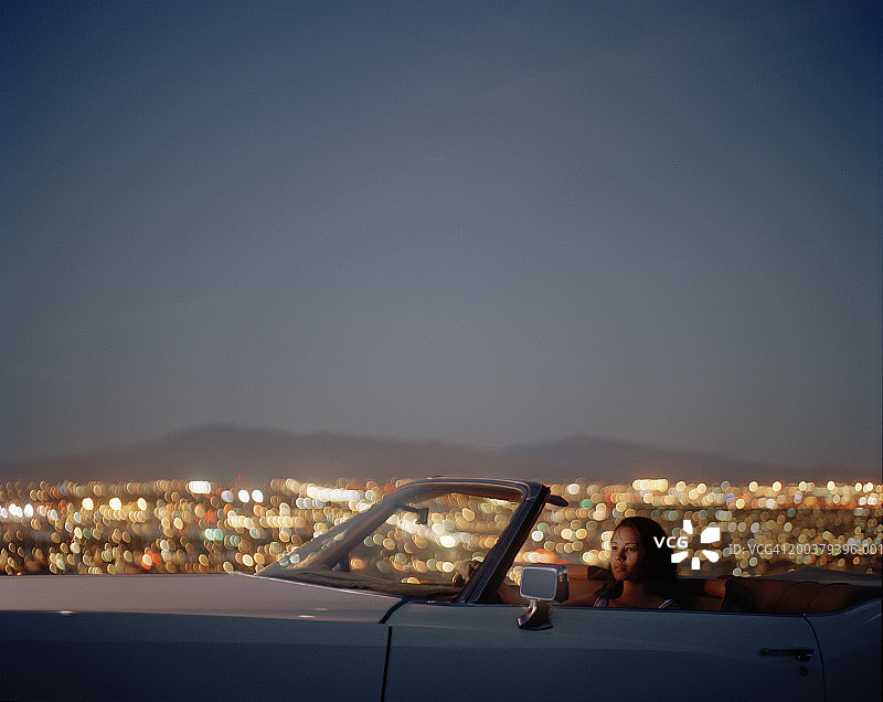 年轻女子坐在敞篷车里俯瞰城市，侧视图图片素材