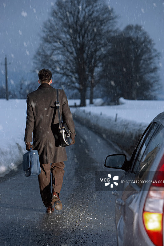 黄昏时分，商人走在雪地上的乡间小路上，前景是一辆汽车图片素材