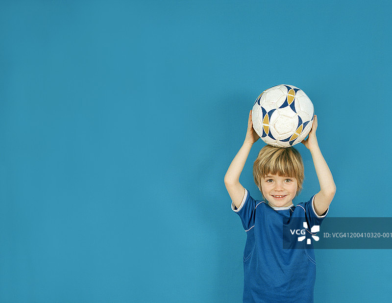 男孩(4-6)头顶球，面带微笑，肖像图片素材