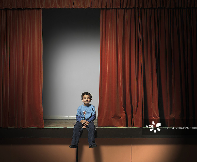 男孩(5-7)坐在舞台边缘，拿着奖杯，肖像图片素材