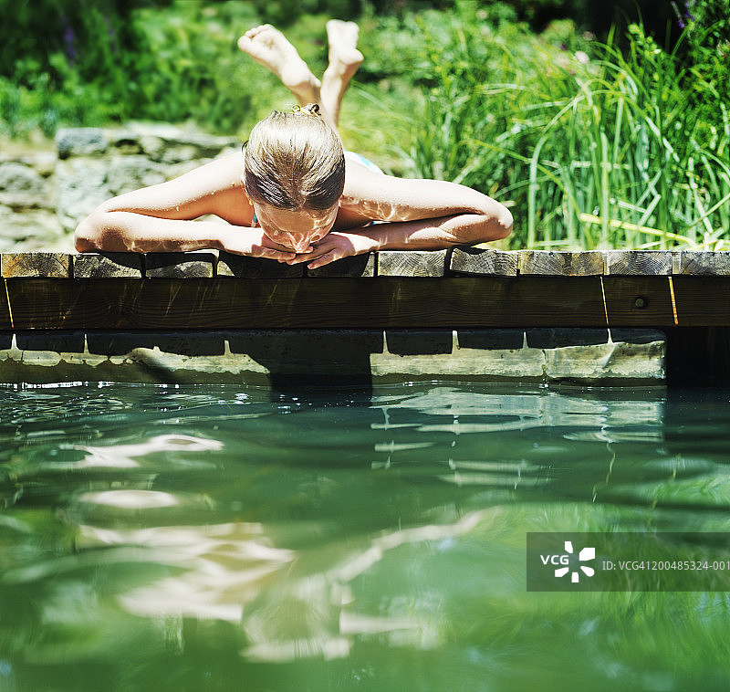 女孩(10-12)躺在防波堤上，看着池塘里的倒影图片素材