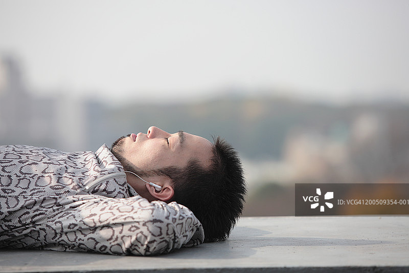 年轻人躺在建筑物边缘，戴着耳机，侧视图片素材