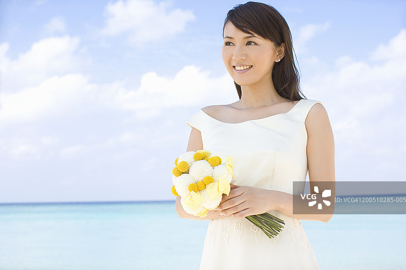 新娘手捧花束，微笑着站在沙滩上图片素材