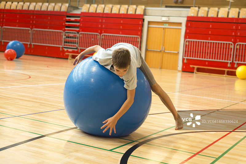 11岁的男孩在学校体育馆玩蓝色健身球图片素材
