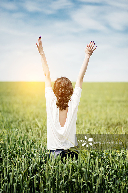 日落时分，年轻女子在草地上张开双臂图片素材