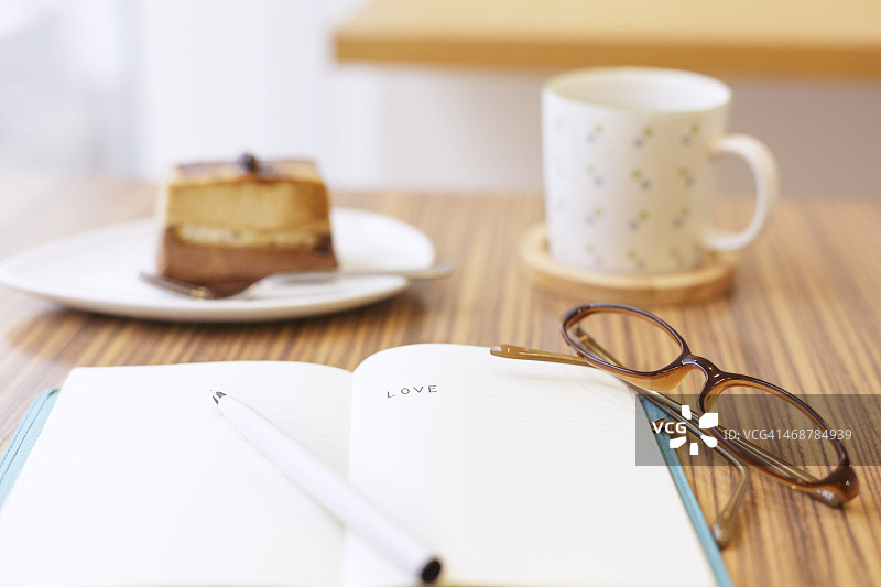 桌上放着记事本，背景是奶酪蛋糕和茶图片素材
