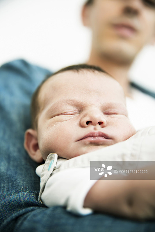 年轻的父亲抱着熟睡的新生儿图片素材