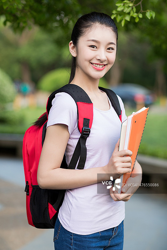 女学生在户外拿着笔记本，面带微笑图片素材