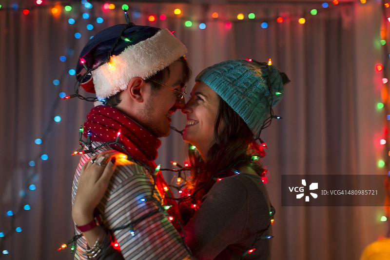 在圣诞节，浪漫的年轻夫妇被装饰彩灯包裹着图片素材