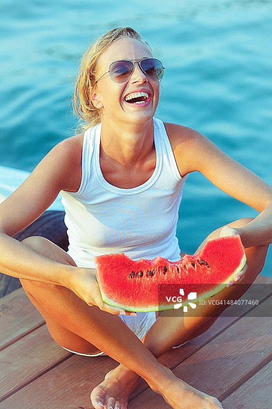 年轻快乐的女人坐在码头上，手里拿着西瓜图片素材