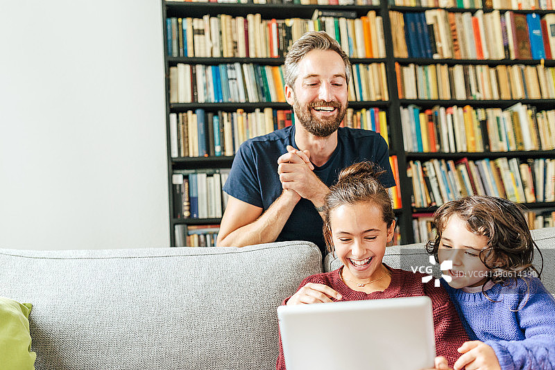 快乐的父亲和两个使用电子平板电脑的女孩图片素材