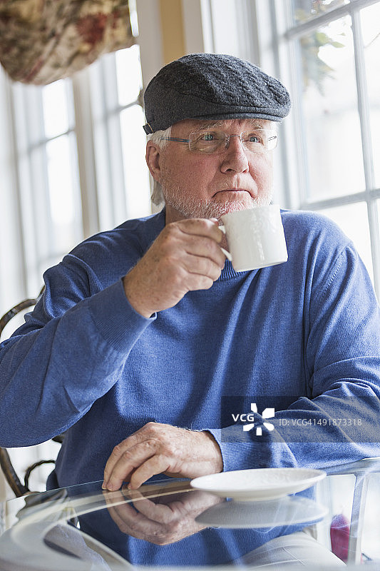一位老人坐在靠窗的桌子边喝咖啡图片素材