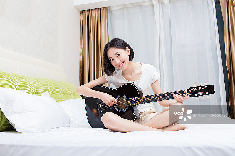 卧室里弹吉他的女孩的肖像图片素材