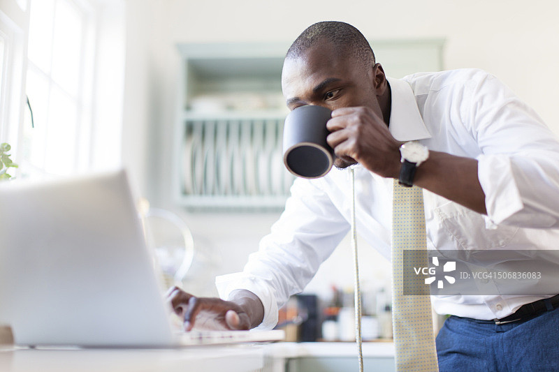 南非开普敦，一名非洲商人在厨房里使用笔记本电脑和喝咖啡图片素材