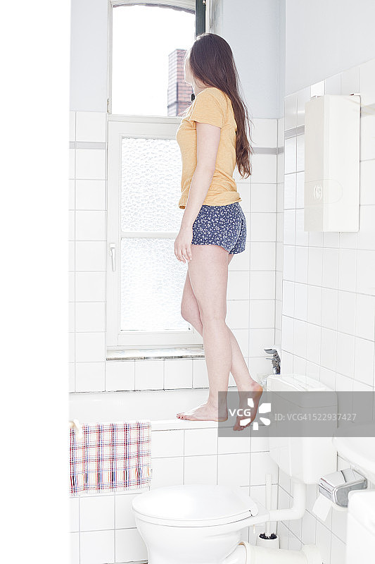 一个年轻女子站在浴室的浴缸边，看着窗外图片素材