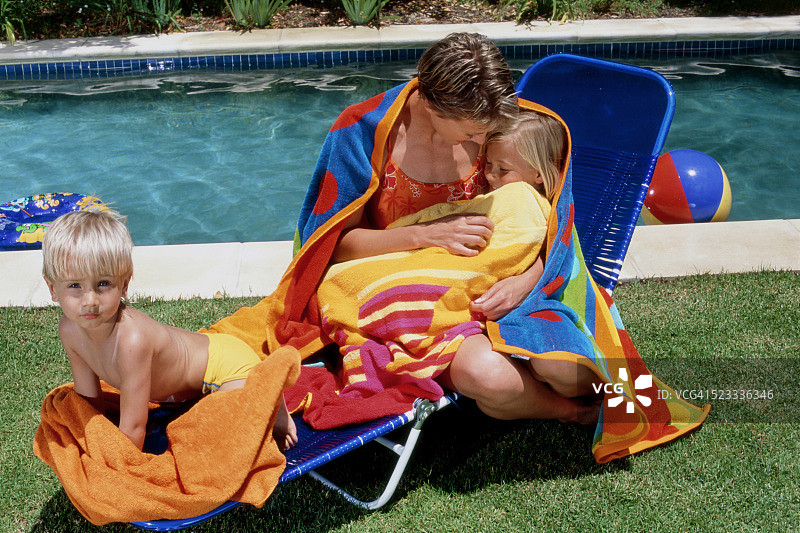母亲和她的两个孩子在游泳池的太阳躺椅上图片素材