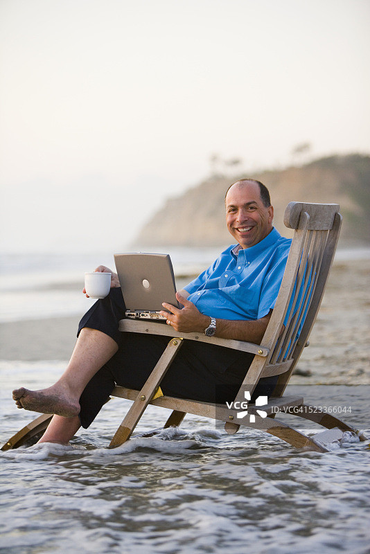 带着笔记本电脑坐在海滩上的普通商人图片素材