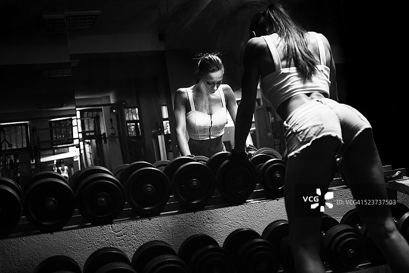 运动员性感女人在健身房做哑铃运动图片素材