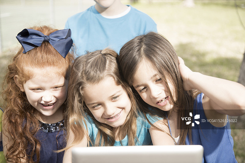 科技:三个女孩在公园和学校里享受户外平板电脑。图片素材