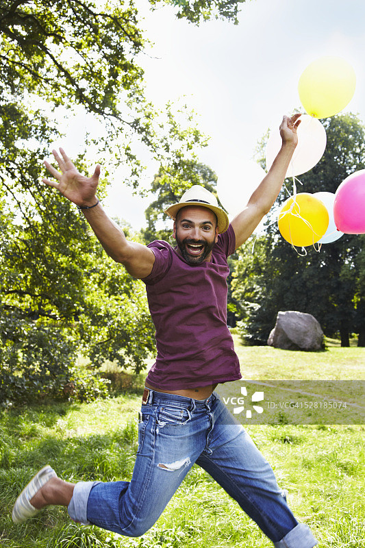 一个男人拿着一堆气球在公园里跳图片素材