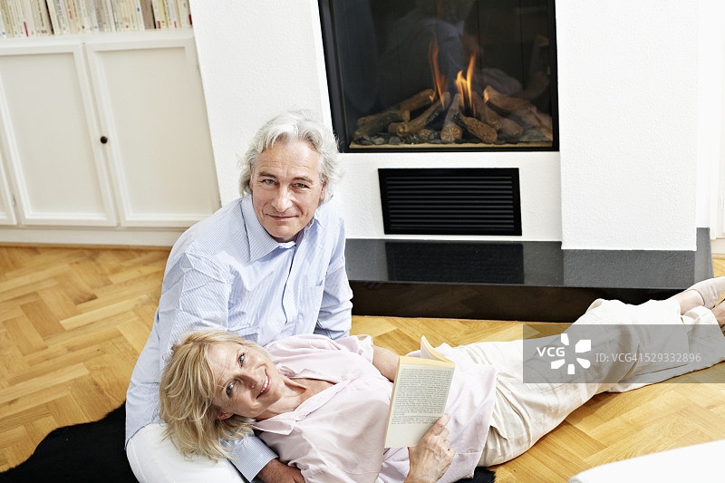 微笑的中年夫妇坐在壁炉前的肖像图片素材