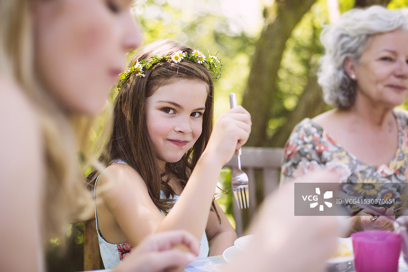 女孩坐在母亲和祖母之间的花园桌子图片素材