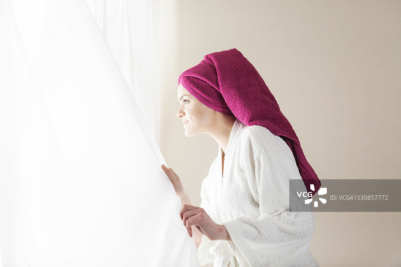 穿着浴袍的年轻女子望着窗外图片素材